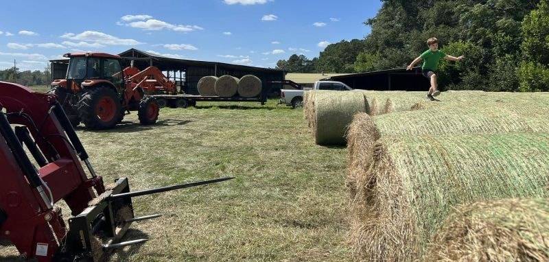 Boy jumping on hay bales with tractor in background